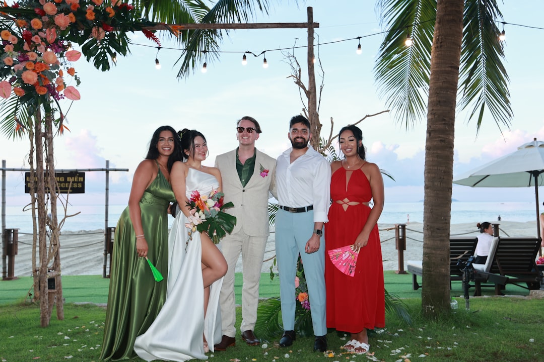 Wedding guests dressed in elegant beach attire watching a sunset ceremony on the sand