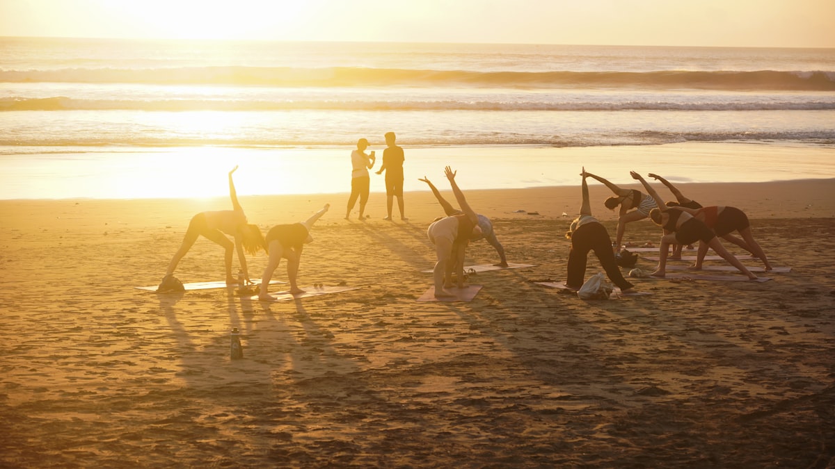 Group practicing beach yoga at sunset in swimwear for outdoor fitness