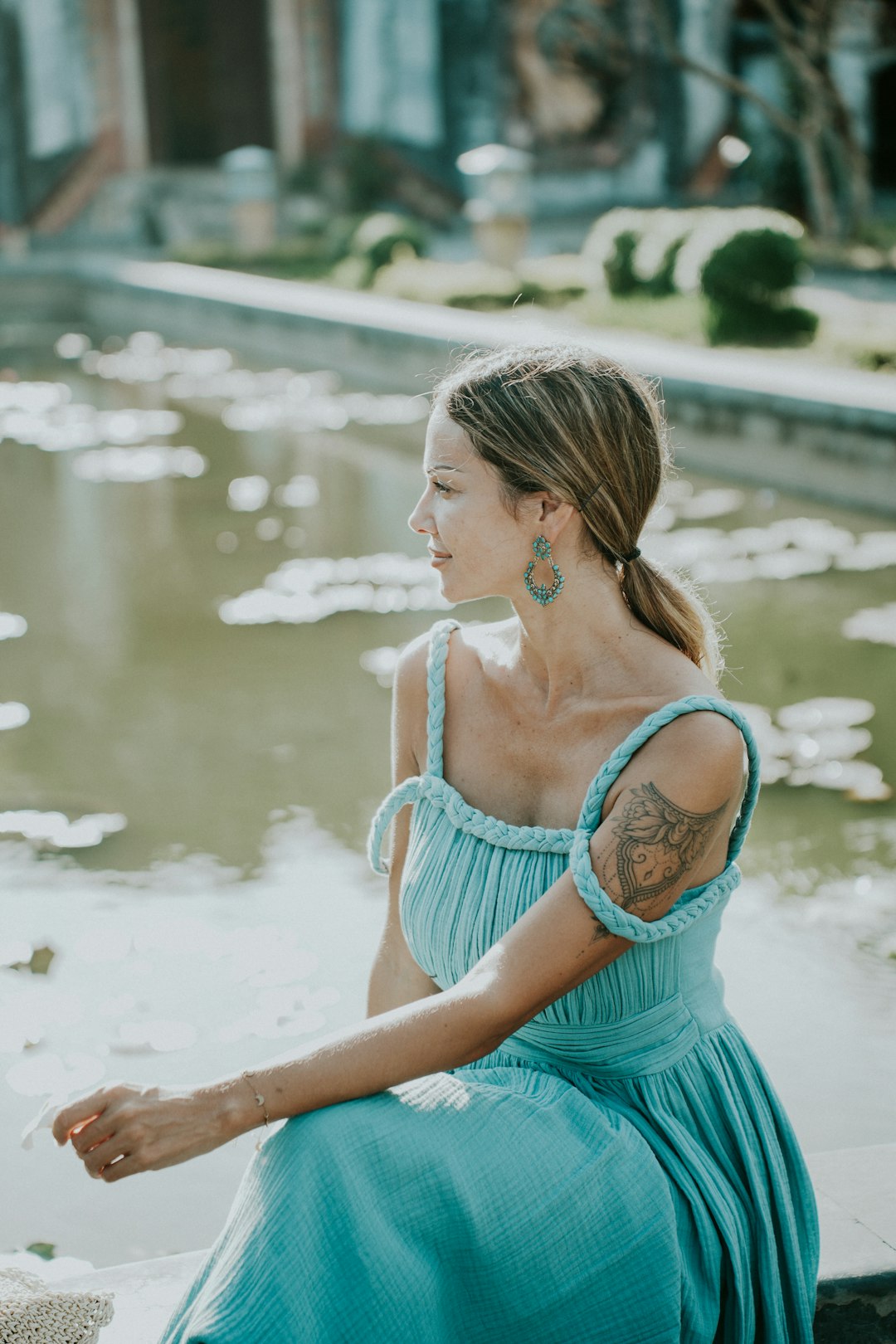 Woman in an elegant blue dress sitting by the water wearing a beach wedding guest outfit