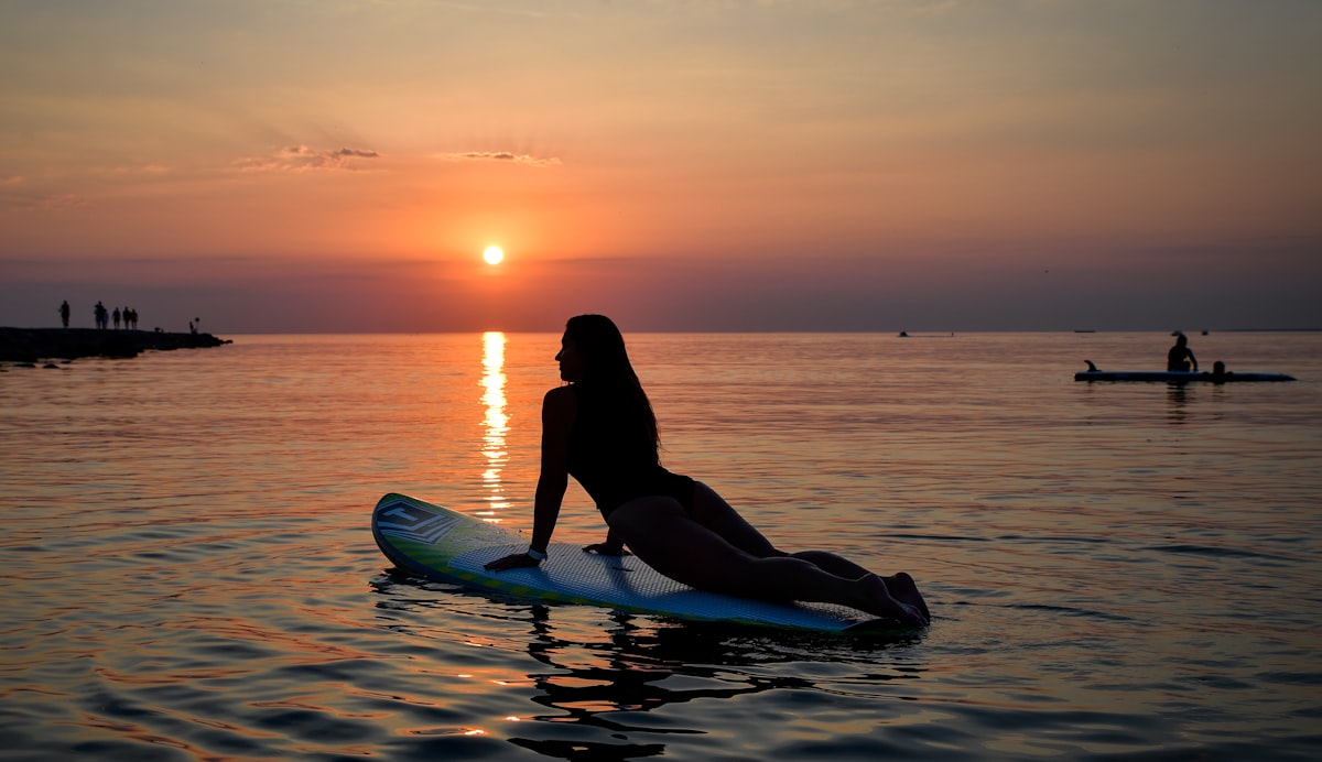 Woman doing yoga on a paddleboard at sunset wearing active swimwear