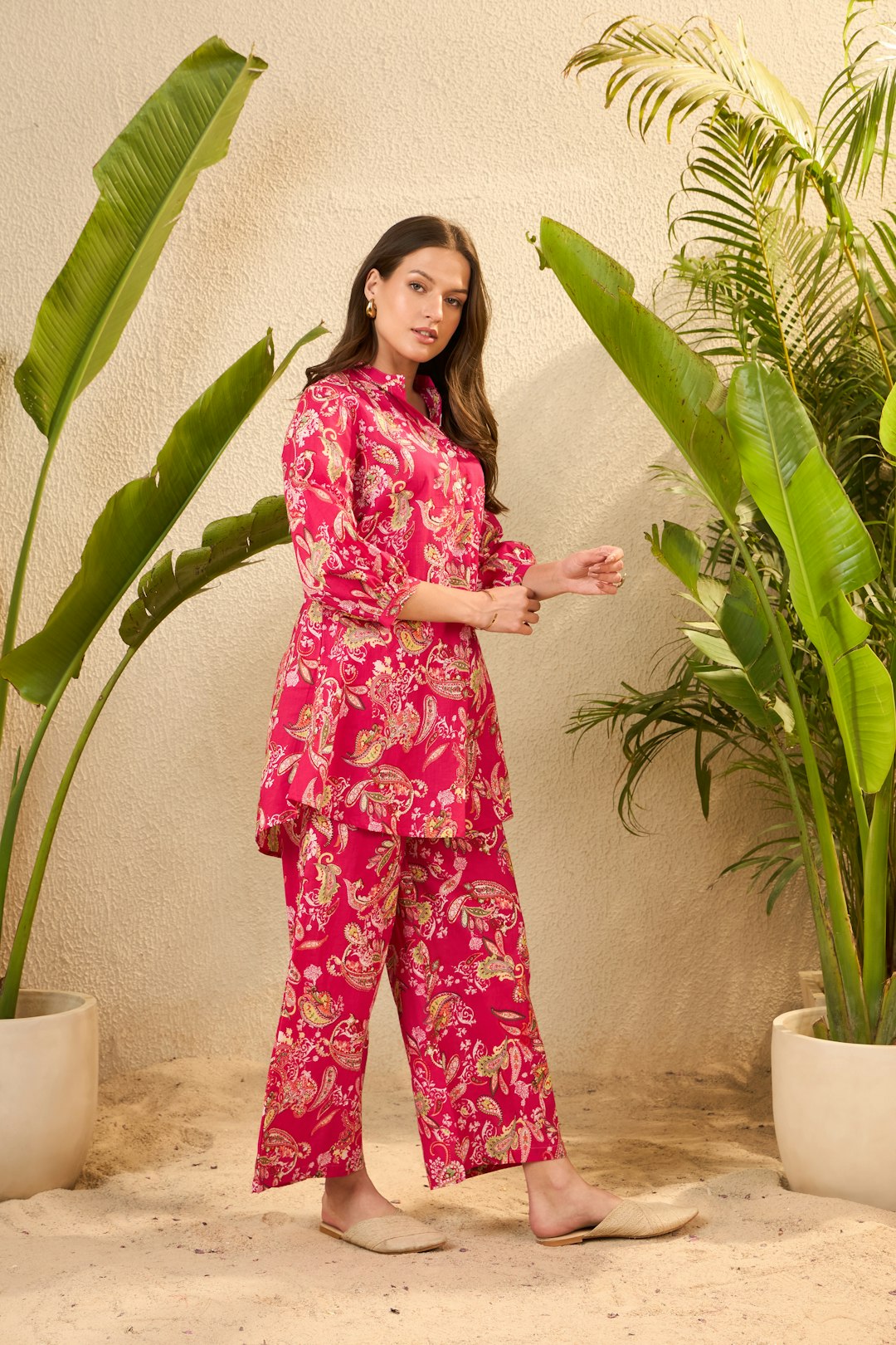 Woman in a pink floral tropical outfit with resort wear accessories near lush tropical plants