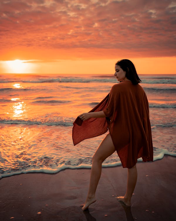 Woman in an orange beach coverup wrap walking along the shore at sunset