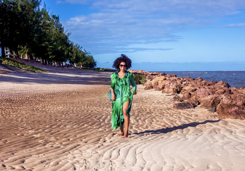 Woman in green flowing beach cover-up dress walking on tropical beach resort summer 2026
