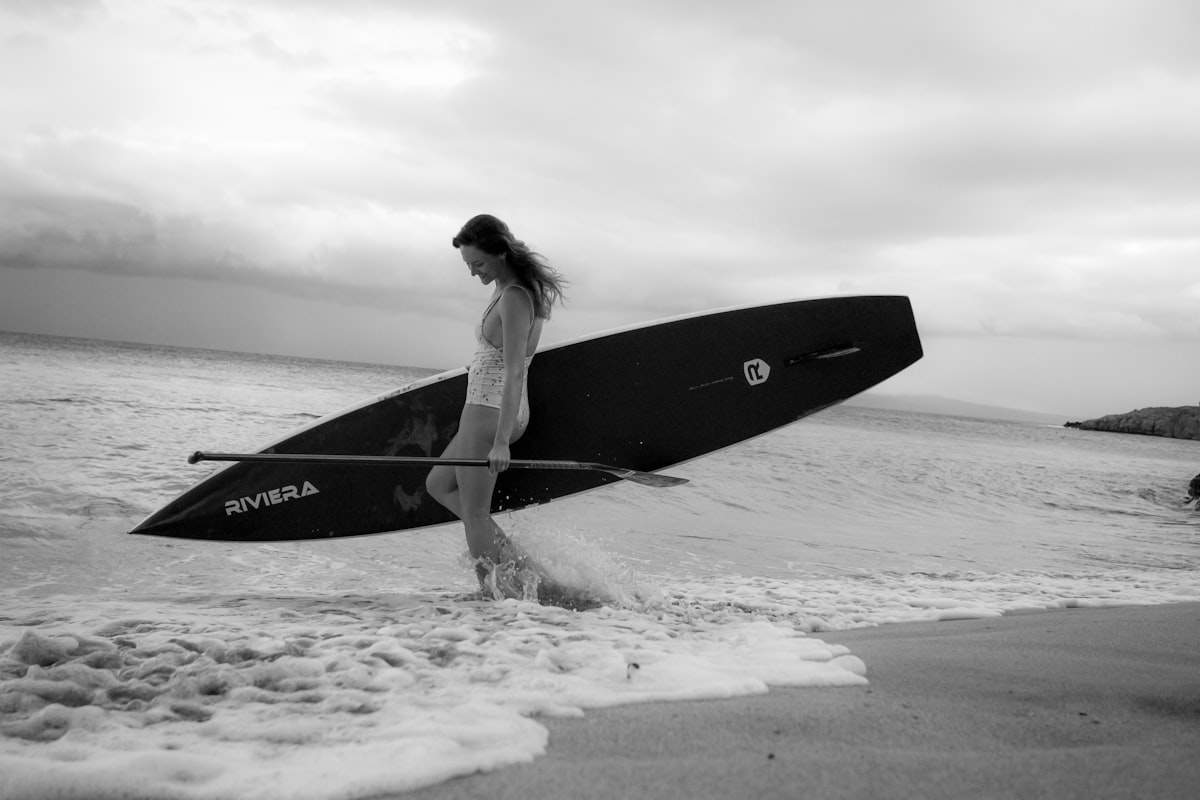 Woman walking on beach carrying a paddleboard in active swimwear