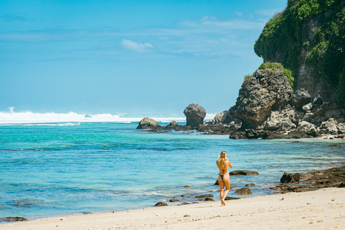 Woman walking along a tropical beach near dramatic cliffs wearing summer swimwear