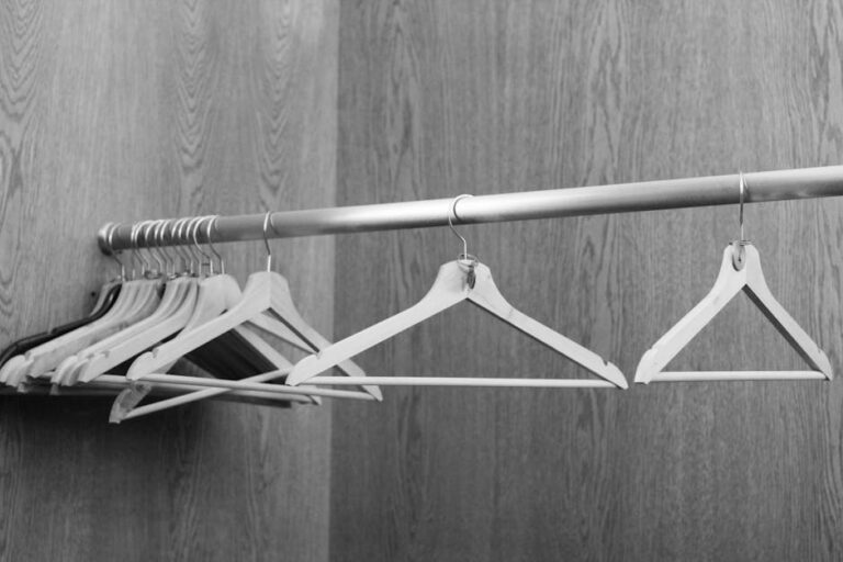 Black and white image of clothes hangers on a rod against a wood-paneled wall.