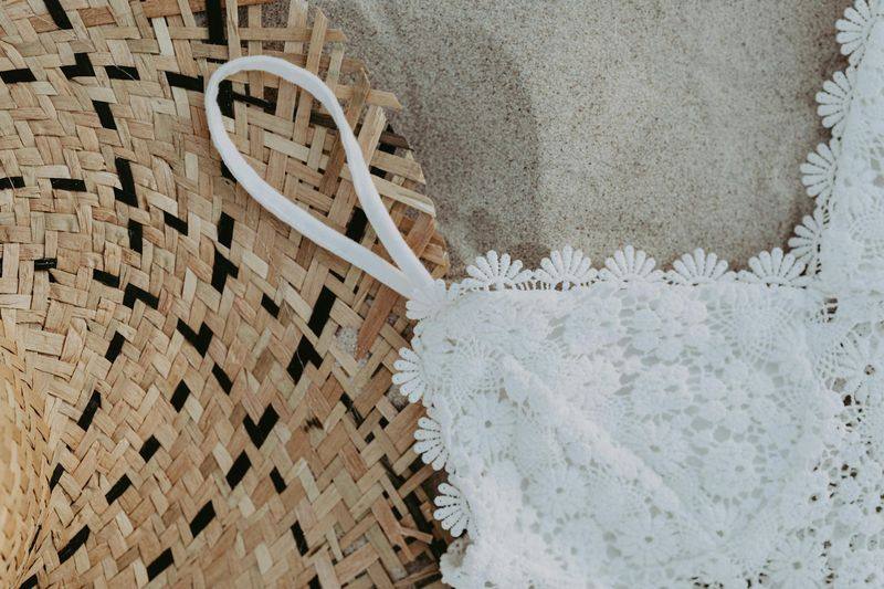White crochet bikini top flatlay with woven straw hat accessory