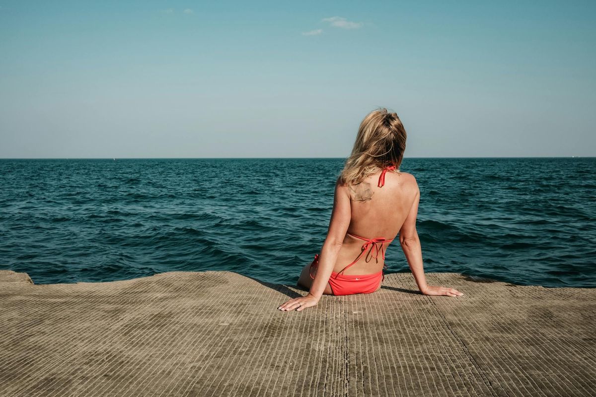 tankini swimsuits 2026 woman seated by ocean in red tank-style swim top
