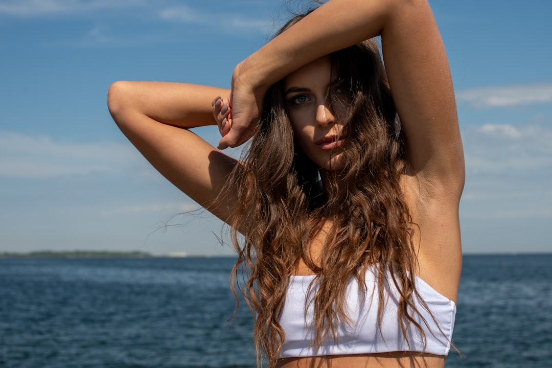 "A confident young woman in a sleek white bikini posing against the backdrop of the Baltic Sea at Linnahall, Tallinn, capturi