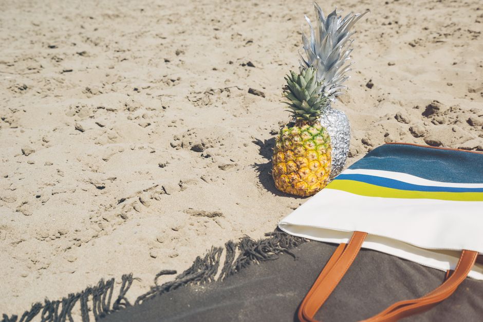 A stylish pineapple with tote bag on a sandy beach, perfect for a sunny day relaxation scene.