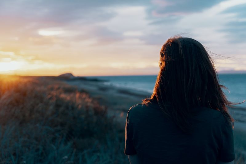 Woman watching a beach sunset feeling beach-body confidence in her swimsuit