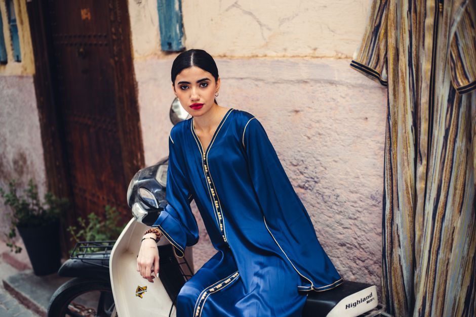 Woman in a blue embroidered kaftan in a sunlit Mediterranean street