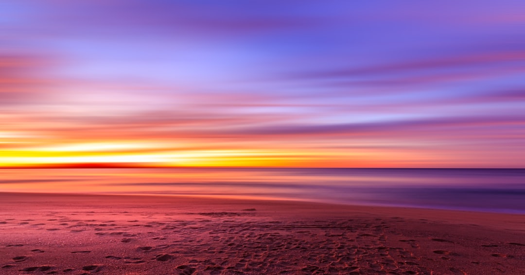 Colorful sunset over a calm beach with soft sand in the foreground
