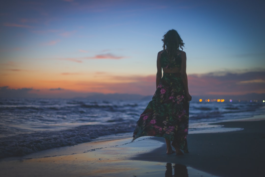 Woman in a floral maxi beach dress walking along the shore at sunset