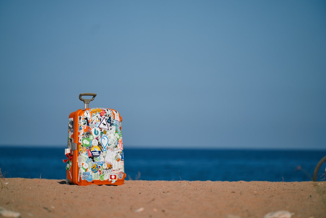 Orange traveler suitcase in stickers, europe travel, suitcase on the beach. Summer time Eurotrip