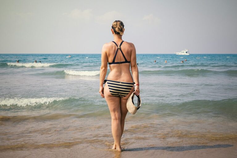 Woman in a striped bikini facing the sea showing flattering apple shape swimwear style