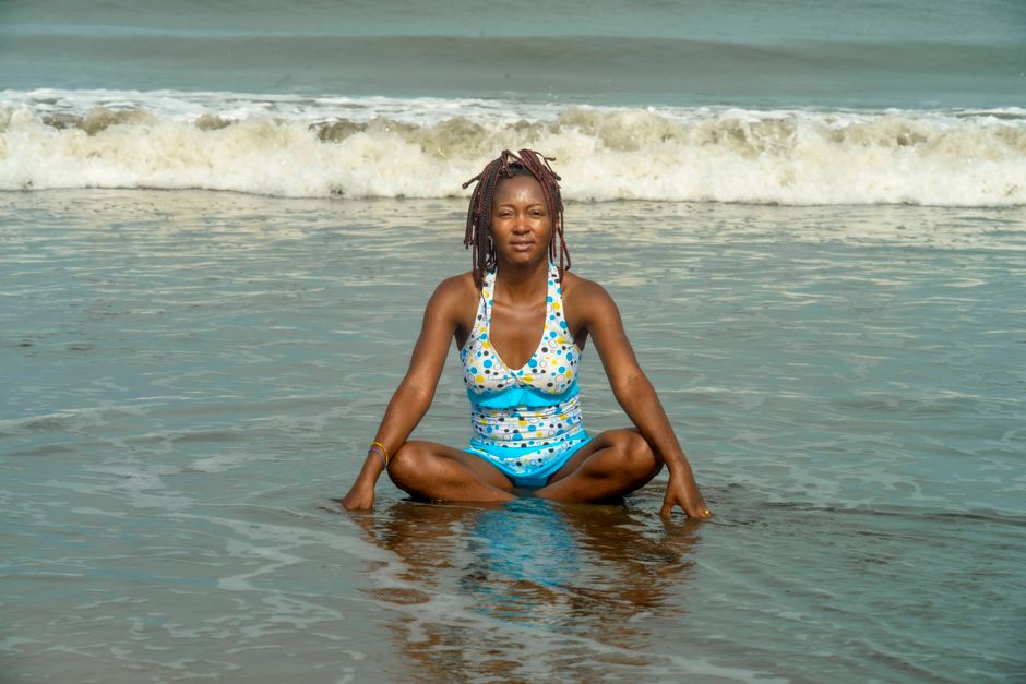 A black woman enjoying a relaxing moment on the beach, sitting by the sea's edge with waves in the background.