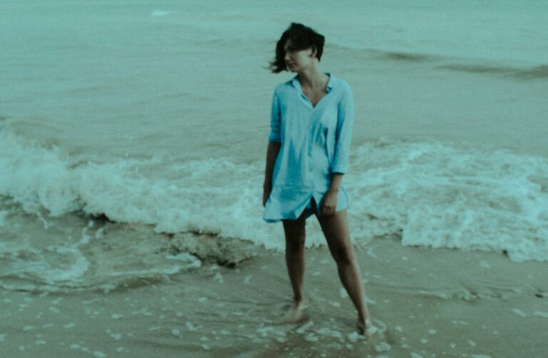 Woman wearing oversized linen button down swim cover up walking through ocean waves 2026