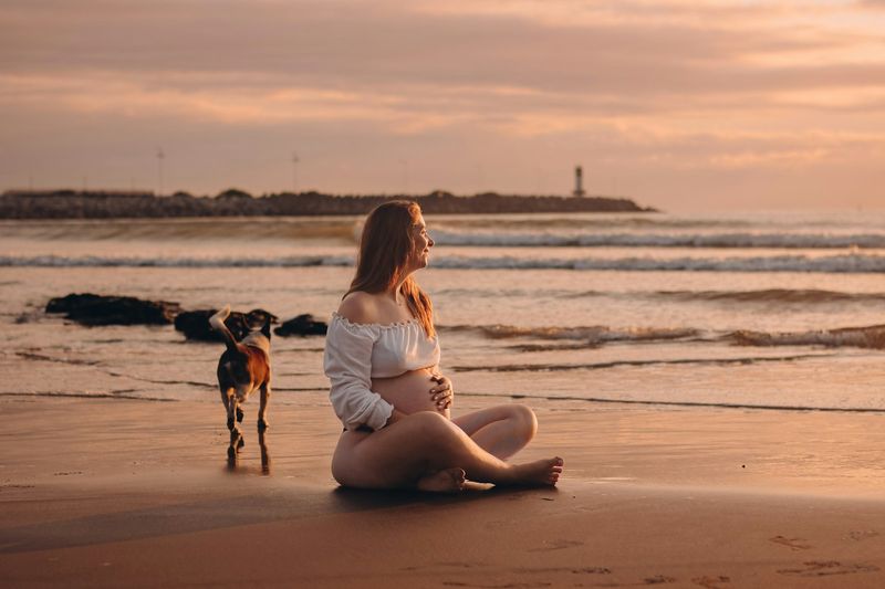 Pregnant woman in a cropped white maternity swimwear top at sunset showing her bump on the beach