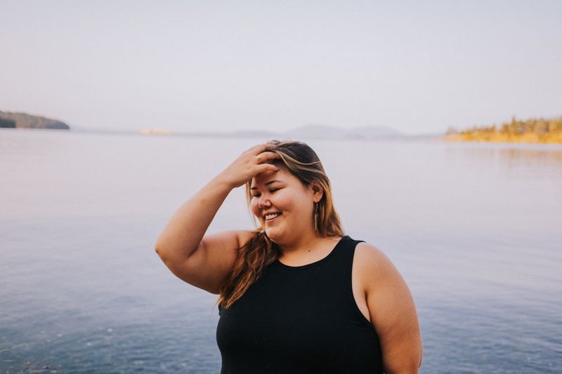 Plus-size woman smiling in a black swimsuit chosen for her body type by the water
