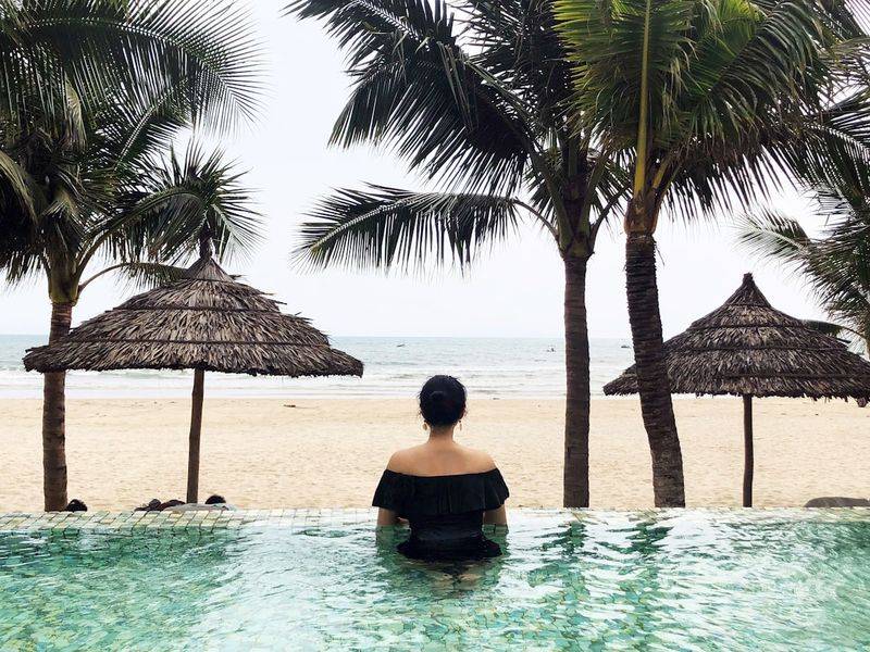 Woman in poolside cover up relaxing by infinity pool ocean view