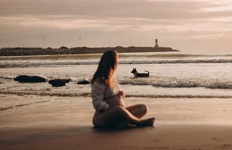 Third trimester pregnant woman in maternity swimwear sitting on the beach at golden hour