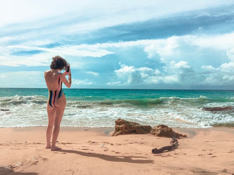 Woman in supportive striped swimsuit photographing the sunset beach