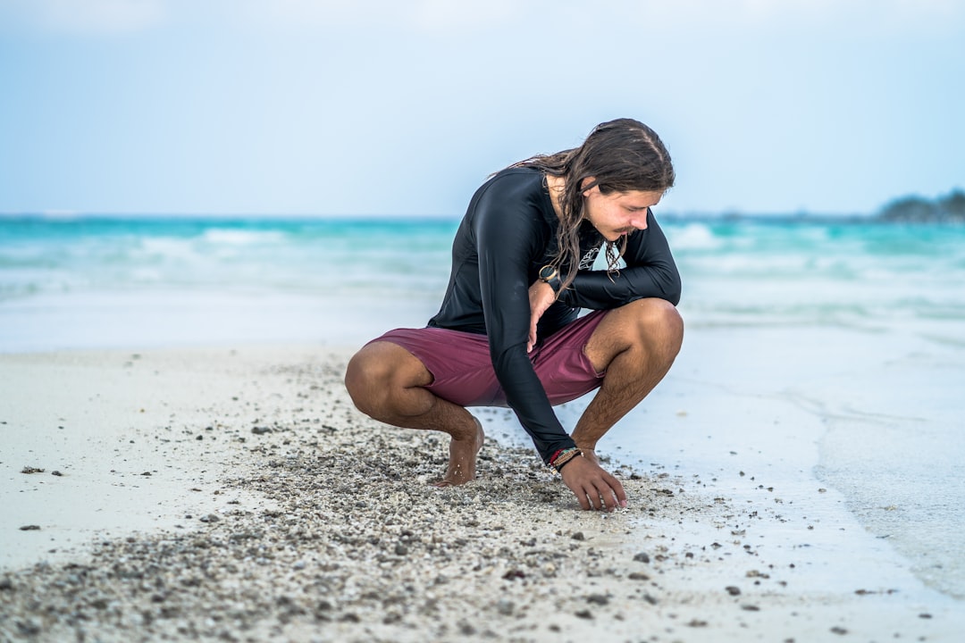 Man crouching on a sandy beach by the ocean.