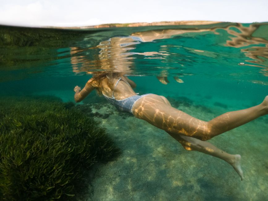 A woman swims underwater in a crystal clear sea, showcasing marine life and tranquility.