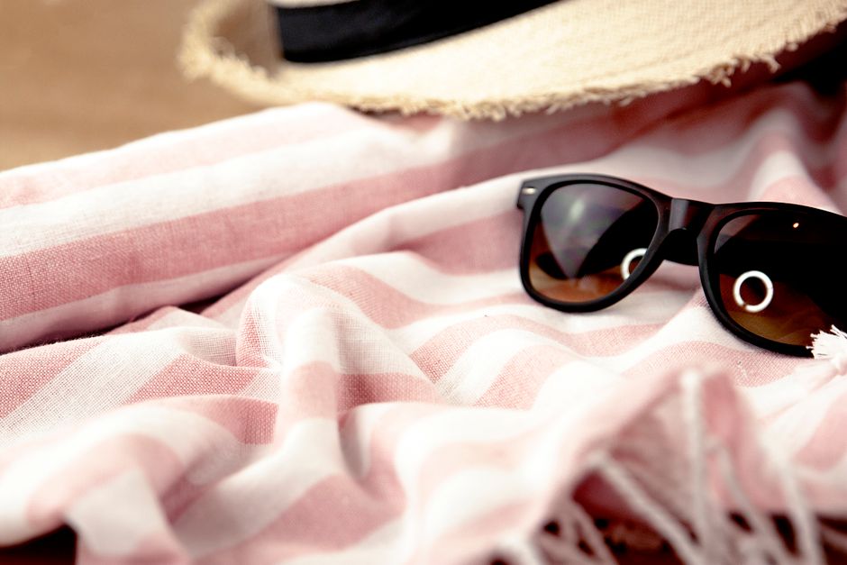 Close-up of sunglasses and a hat on a striped beach towel, perfect for summer leisure.