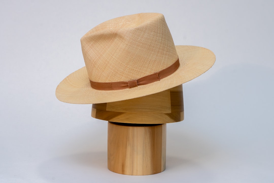 A classic straw Panama hat with a caramel-brown band rests on a sculptural wooden display, captured in soft studio lighting a