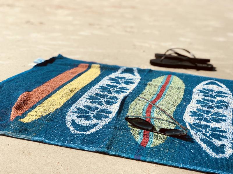 beach bag packing essentials with towel and sunglasses on the sand