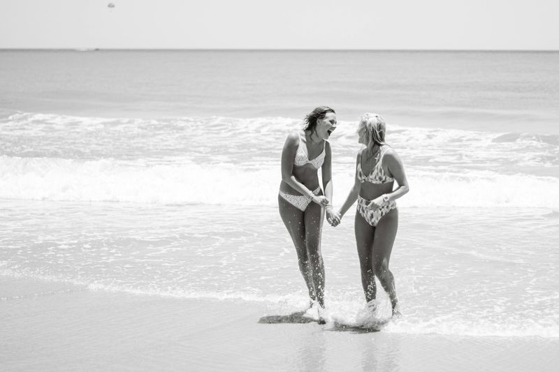 Confident women in bikinis laughing in the surf, representing body positive swimwear styling