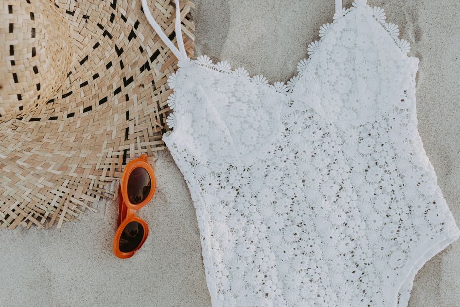 A lace swimsuit with a straw hat and sunglasses on the sandy beach, captured in a top view.