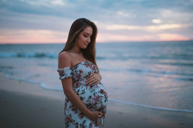 Pregnant woman in floral maternity swimwear on the beach at sunset