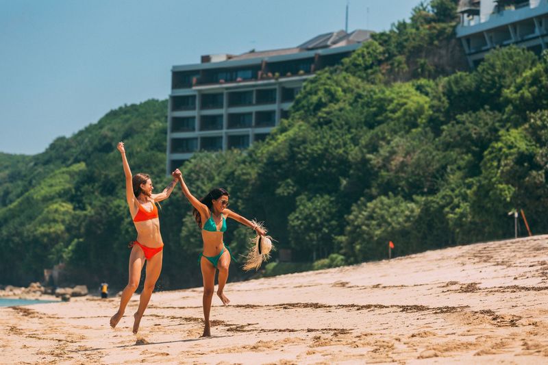 Two women in mix and match bikinis running on sunny beach