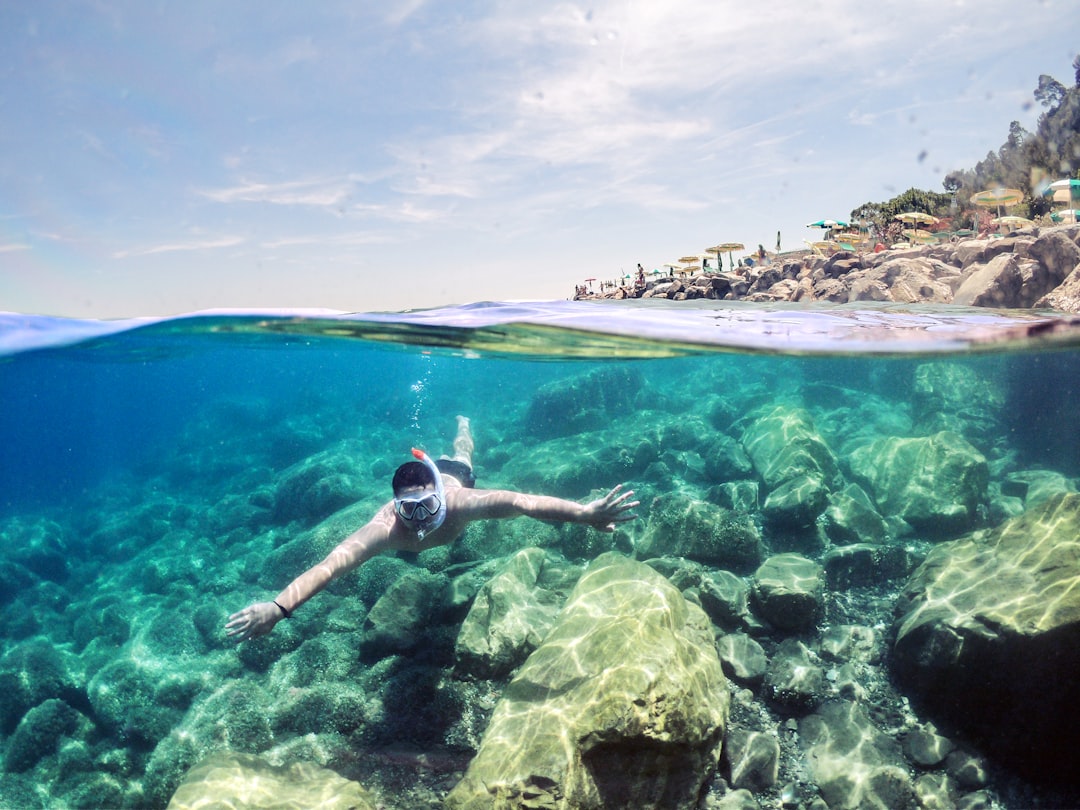 Snorkeler in a fitted swimsuit gliding underwater over rocks in clear sea water