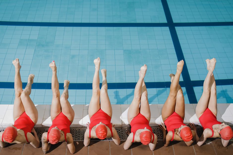 Aerial view of women swimmers in red swimsuits relaxing poolside, legs in water.