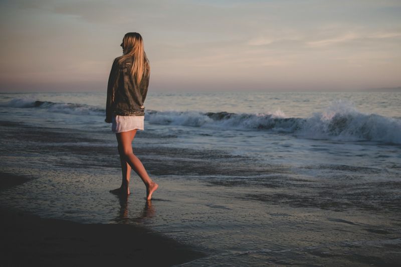 Woman walking along the shoreline in a beach cover-up to prevent thigh chafing