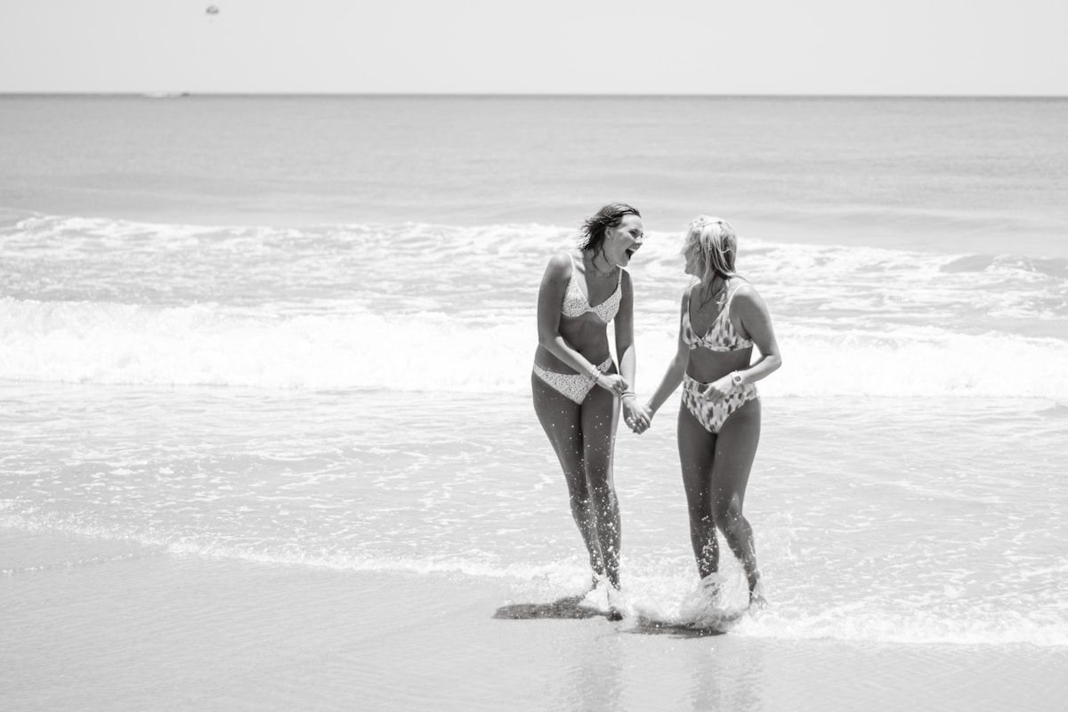 Two women laughing in the surf in swimsuits, swimsuit care guide