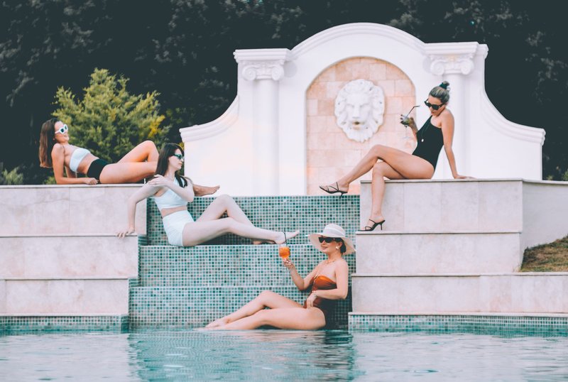 Group of women wearing different swimwear styles by luxury pool