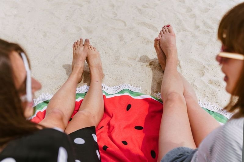 women relaxing at sandy beach in swim shorts style on watermelon towel