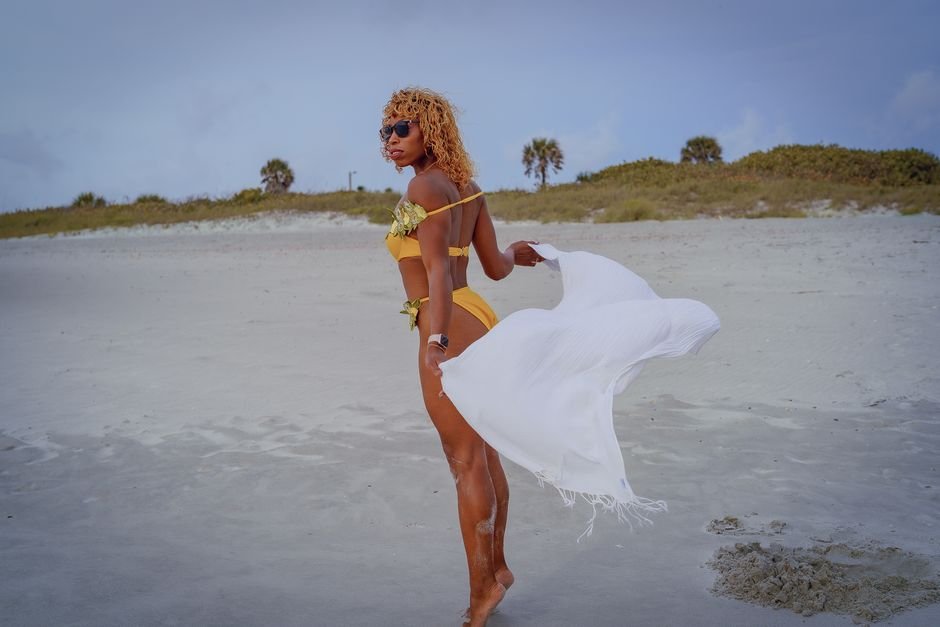 Fashionable woman in yellow bikini with white towel on a sandy beach, posing confidently.