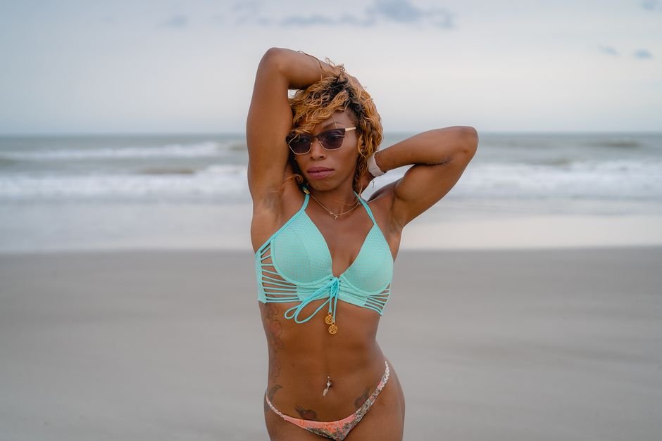 A young woman in a bikini enjoys the beach, with arms raised, exuding confidence.
