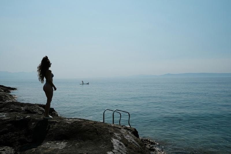 Woman in a ruched swimsuit on a rocky shore overlooking the sea