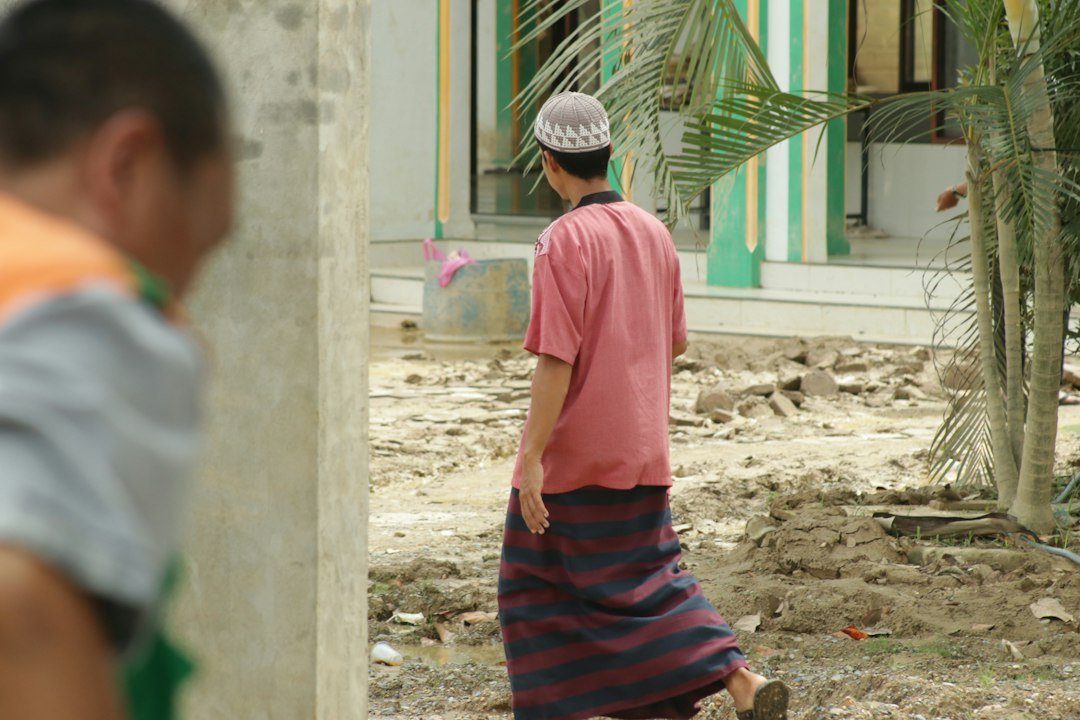 Man in pink shirt and sarong walking on muddy ground