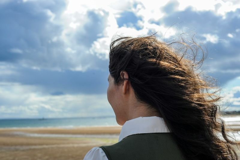 Woman with hair and fabric blowing in strong wind on a windy beach