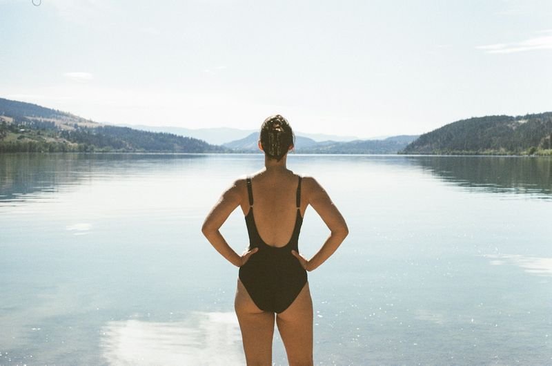 Woman in a black one-piece swimsuit standing at a mountain lake