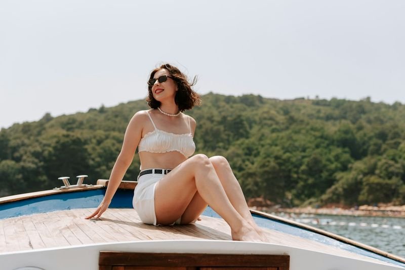Woman in a white two-piece swimsuit sitting on the bow of a boat