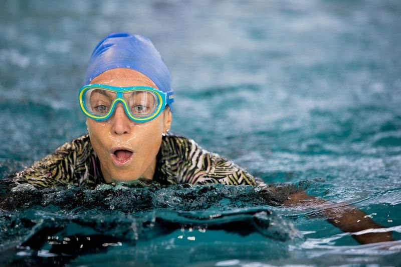 woman swimming with blue cap and goggles in a pool